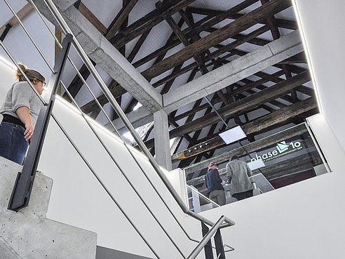 Blick aus dem Erdgeschoss über das Treppenhaus in das Obergeschoss mit sichtbaren, instandgesetzten Dachstuhl im Hintergrund.